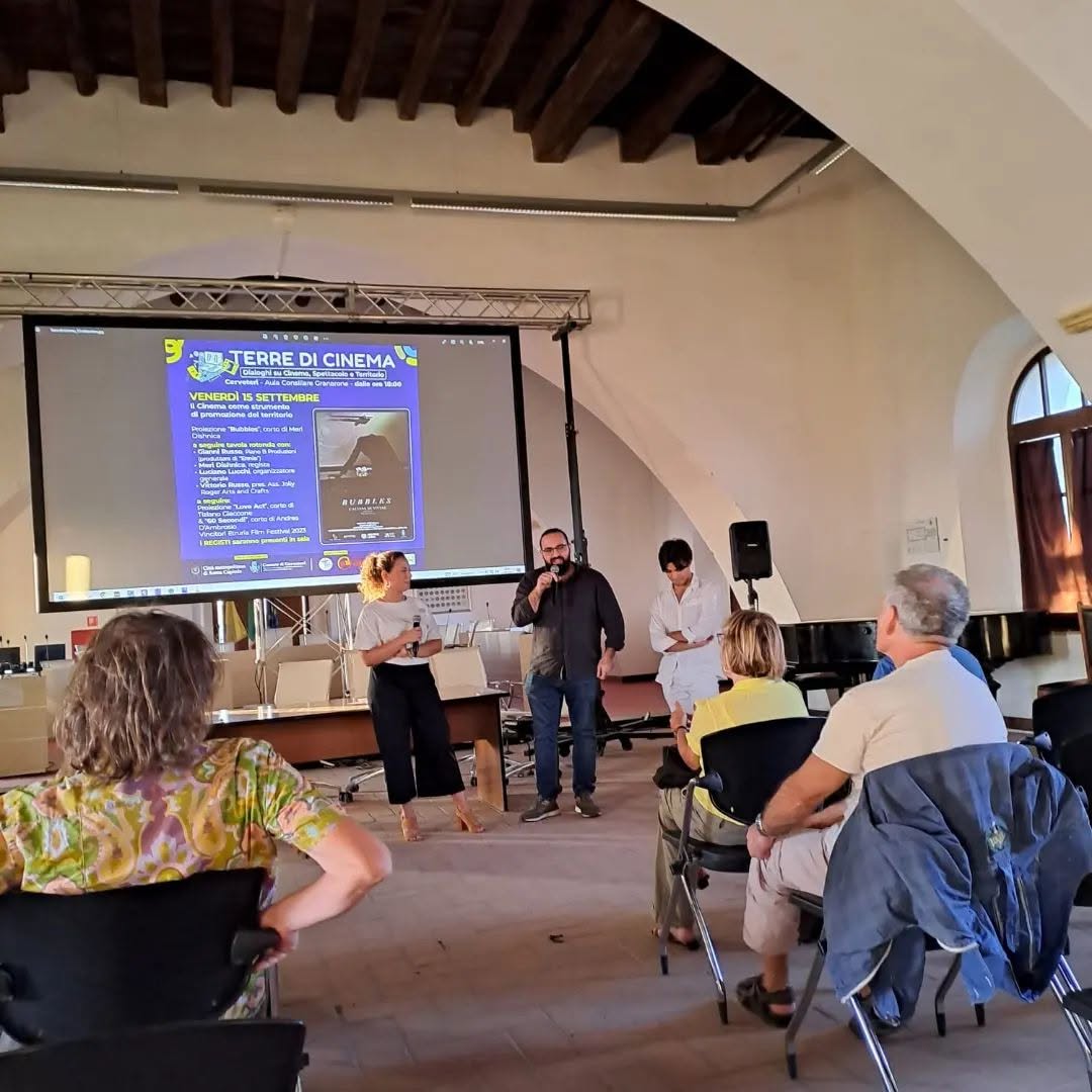 Vittorio Russo holds a microphone in a hall, with the audience in the foreground and a screen reading "TERRE DI CINEMA" and "VENERDÌ 15 SETTEMBRE".