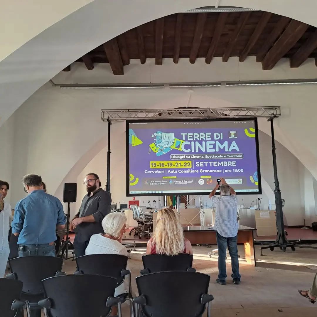 Vittorio Russo, wearing glasses, stands in a hall before a screen reading "TERRE DI CINEMA" and the dates "15-16-19-21-22 SETTEMBRE".