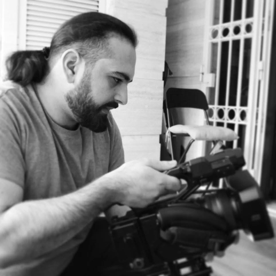 In black and white, Vittorio Russo in profile adjusts a cinema camera resting in the foreground.