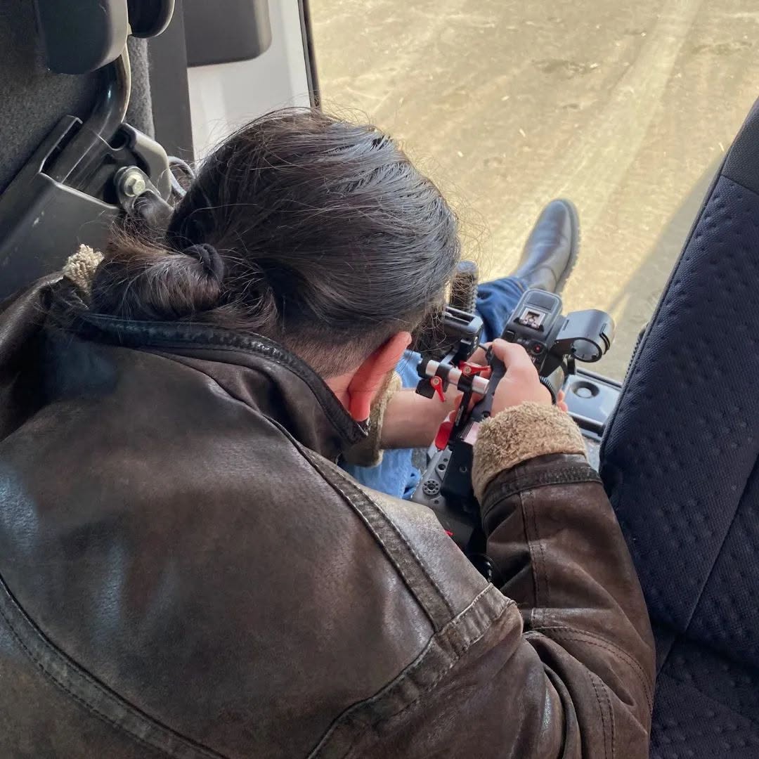 From above, the back of a person's head and their hands adjust a cinema camera inside a vehicle, with the road outside.