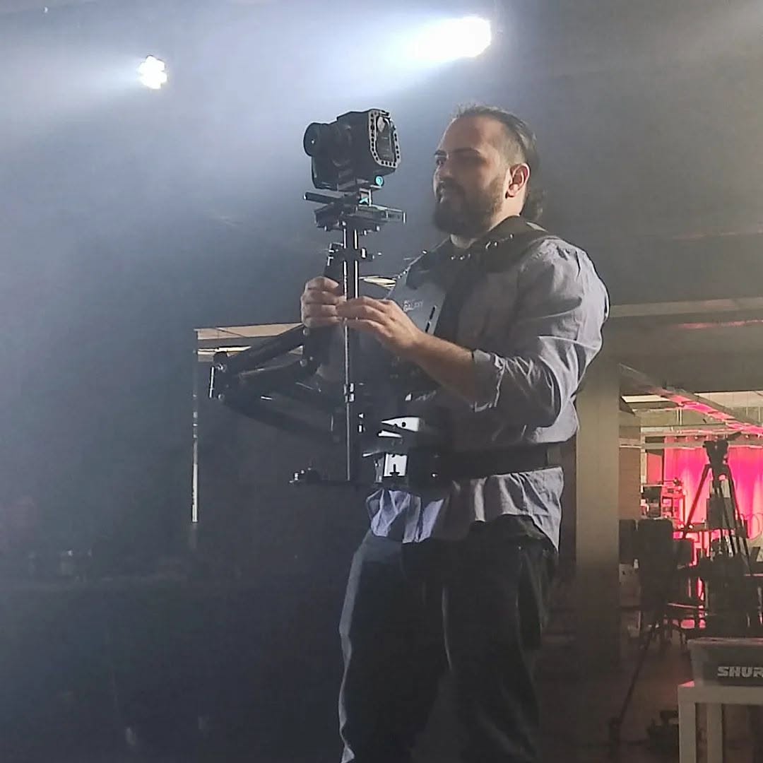 Vittorio Russo, in a support vest, holds a stabilizer with a cinema camera in a dark space under spotlights.