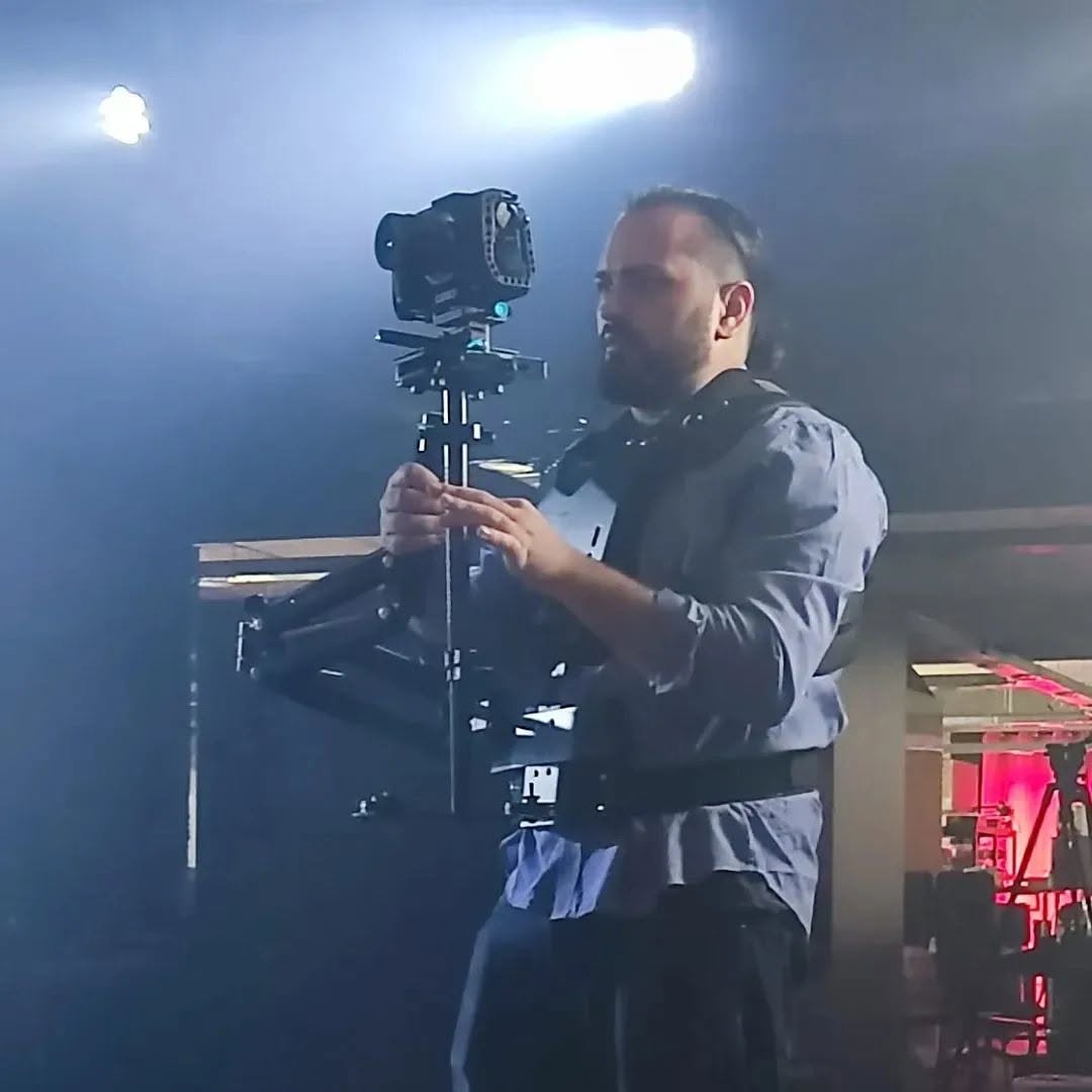 Vittorio Russo adjusts a stabilizer pole with both hands, in a dark interior with spotlights and a tripod.