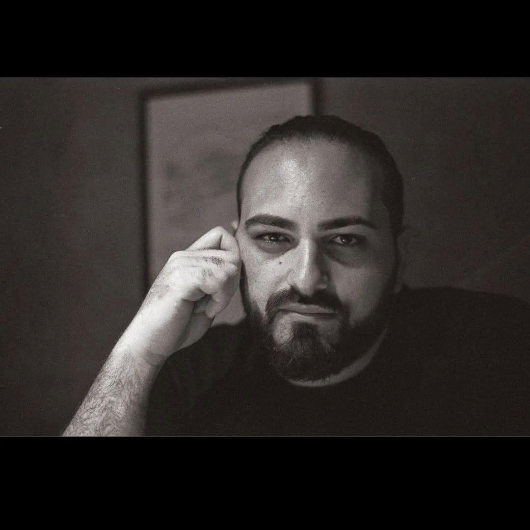 Black-and-white portrait of Vittorio Russo looking at the lens, one hand resting near his ear.