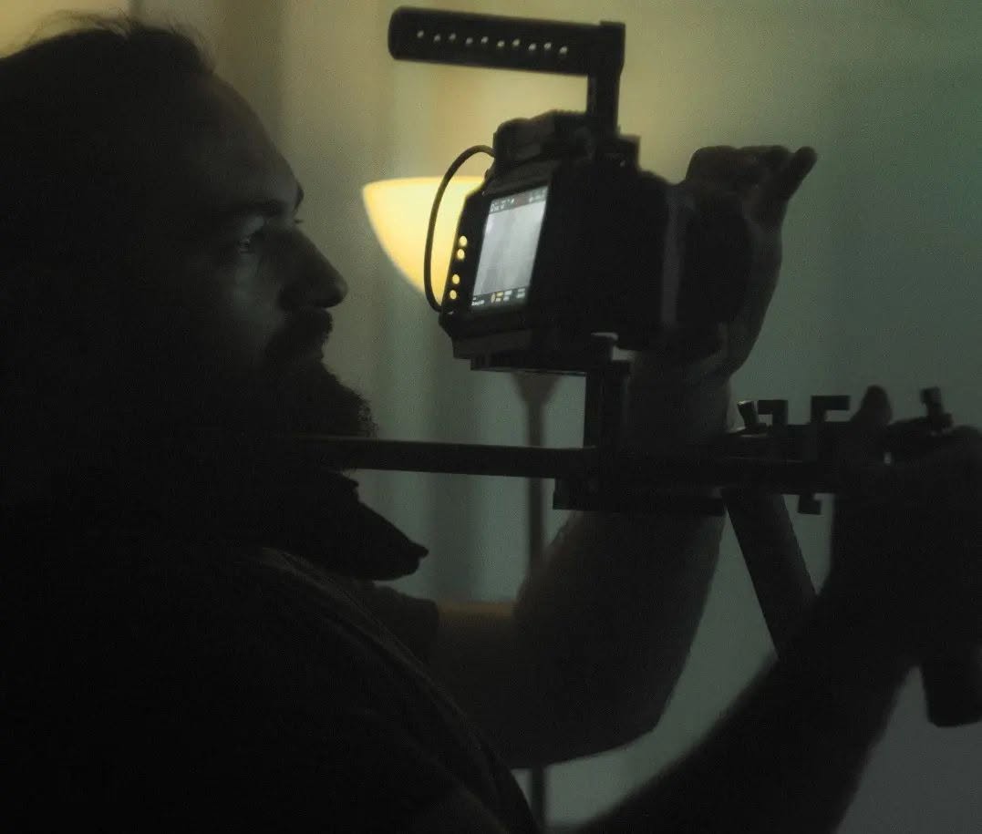 In backlight, Vittorio Russo's profile appears beside a cinema camera on a rig, with a lamp glowing behind it.
