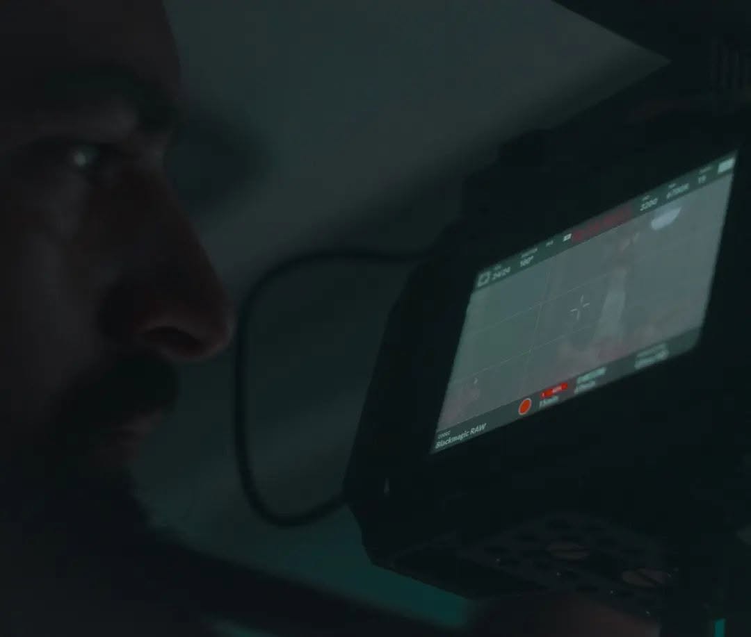 In low light, Vittorio Russo watches in profile a cinema-camera monitor on which “Blackmagic RAW” is readable.