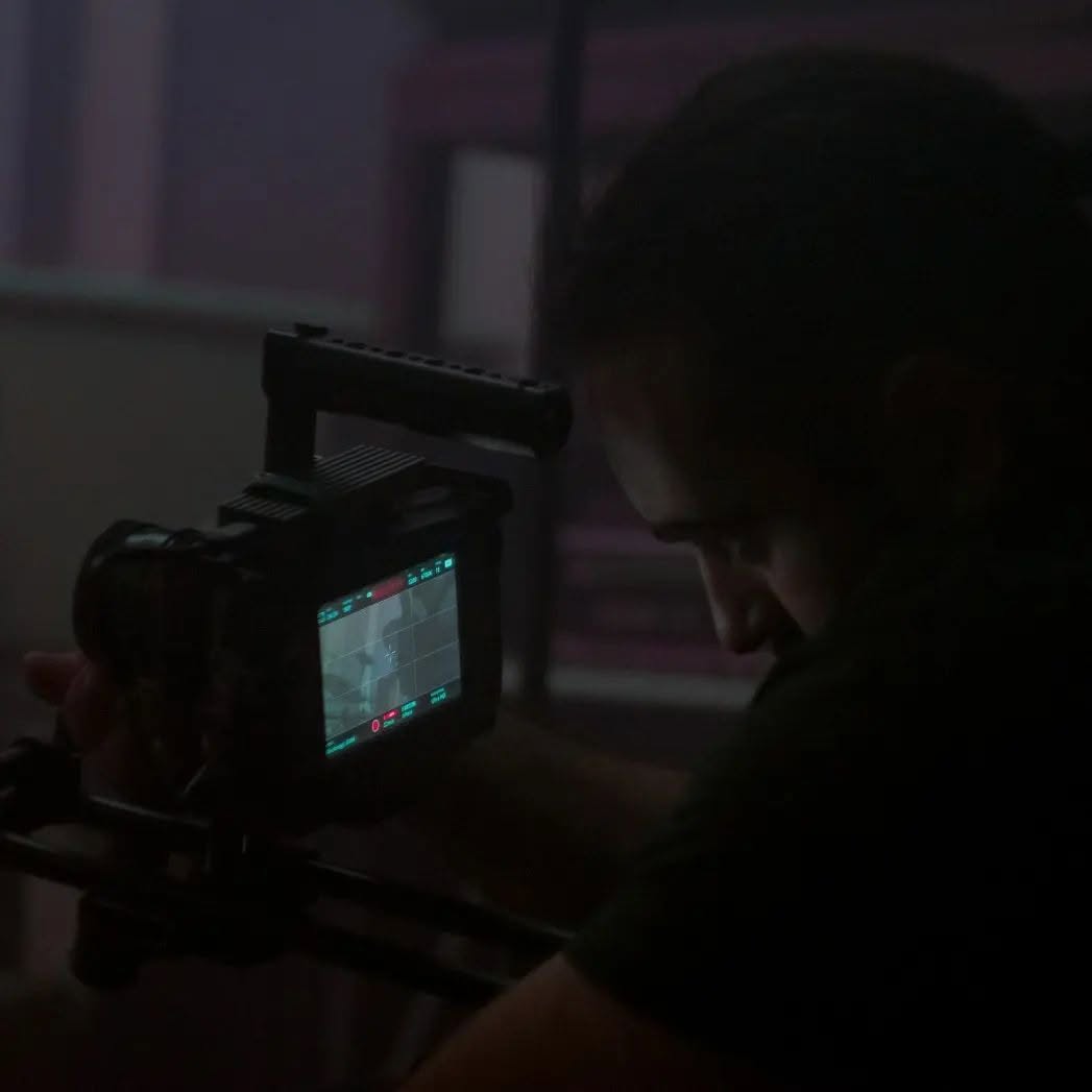 In the dark, Vittorio Russo leans over the lit monitor of a cinema camera fixed to a rig.