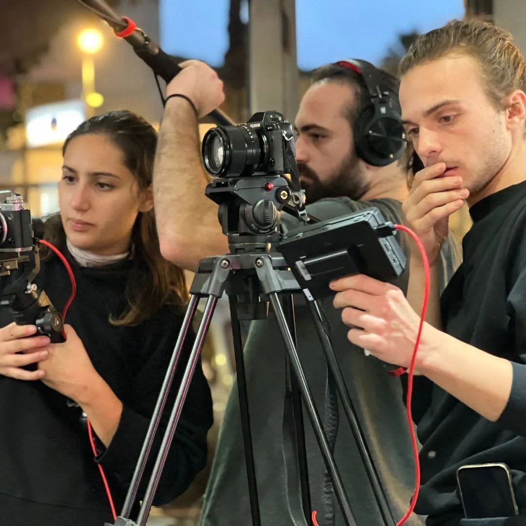 At night, Vittorio Russo in headphones stands behind a cinema camera on a tripod, between two colleagues with other cameras.